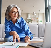 Woman smiling while taking notes next to computer